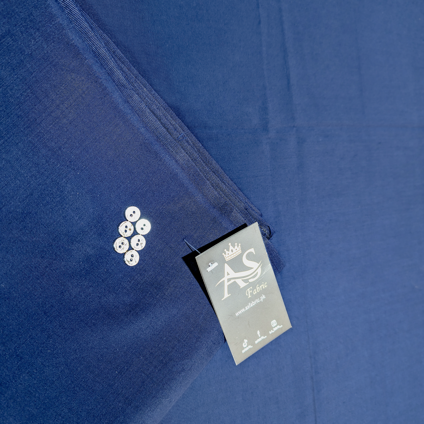 Close-up of a blue shirt with a label and buttons on a matching fabric background